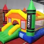 Crayon-themed bouncy castle with colorful design, slide, and mesh sides. Perfect for kids' parties and events. Buy online in Canada today!